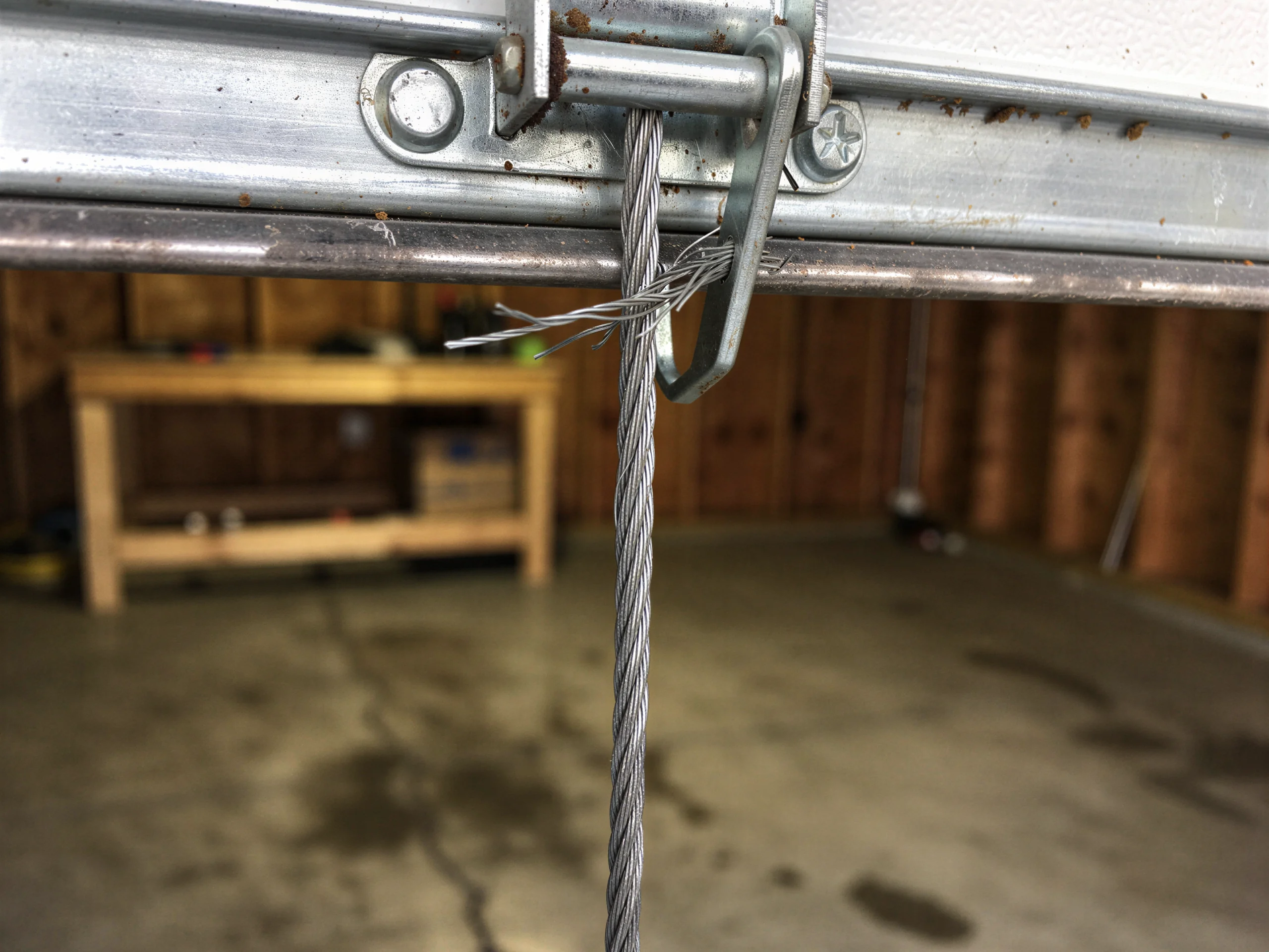 A frayed garage door cable is attached to a metal bracket.